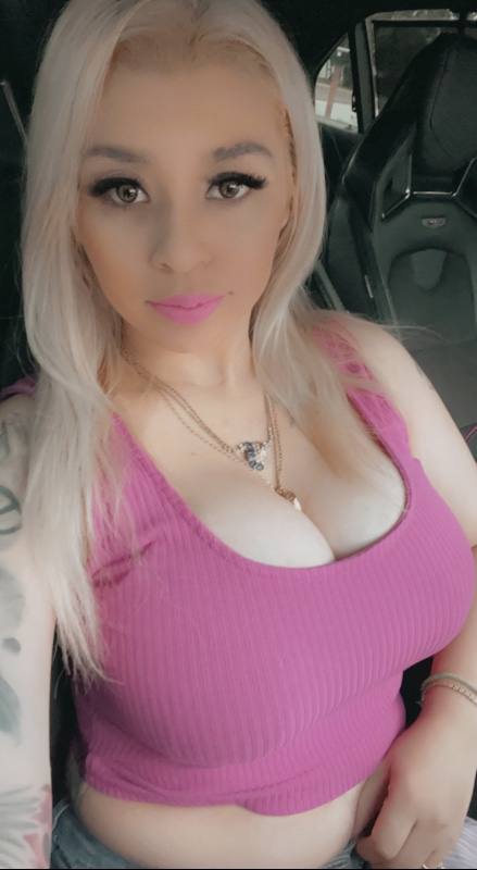 Young woman with platinum blonde long hair, pale complexion, dark winged eyeliner, bright pink lipstick, wearing a pink …